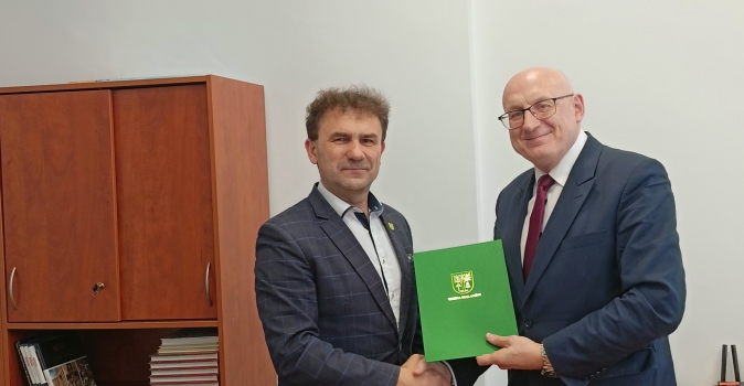 dwoch mezczyzn podaja sobie rece i trzymaja zielona teczke